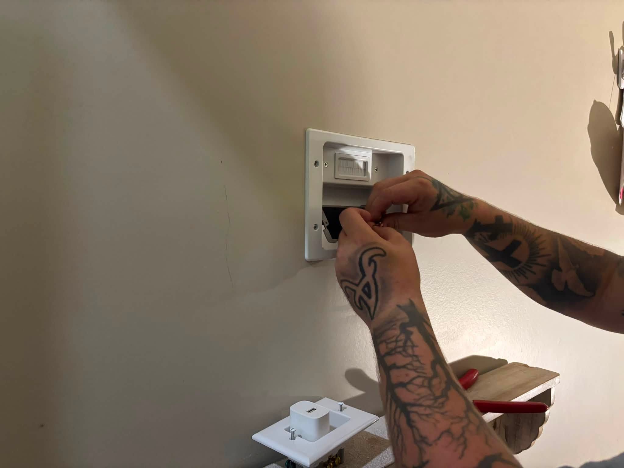 Hands installing a recessed in-wall power and cable plate